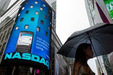 A woman holds an umbrella as she walks past the Nasdaq MarketSite in New York's Times Square