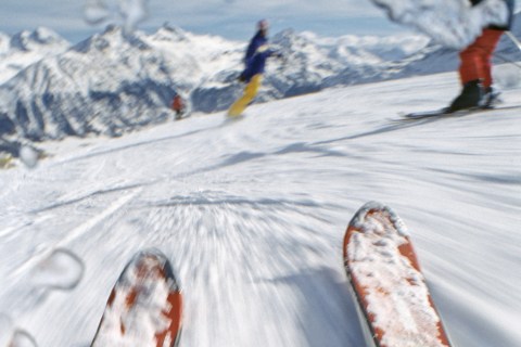 Pair of skis with snow sliding on slope, skiers in background