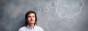 A young man stands in front of a chalk board with a thought bubble above his head.