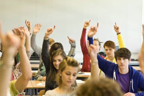 students in classroom raising hands