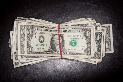 Overhead shot of one dollar bills sitting on a leather background with a red rubber band.