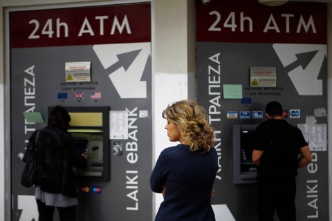 A woman waits as  two people use the ATM machines in central capital Nicosia, Cyprus, on March 22, 2013. 
